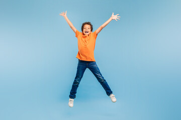 Fototapeta na wymiar Joyful boy jumping with arms wide open on blue background