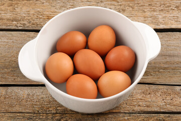 Unpeeled boiled eggs in saucepan on old wooden table, closeup