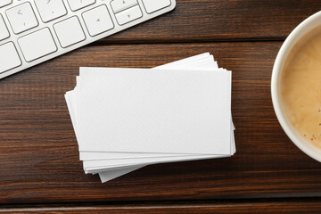 Blank business cards, coffee and keyboard on wooden table, flat lay. Mockup for design