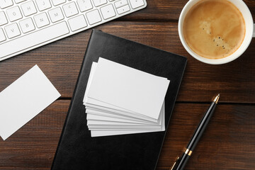 Blank business cards, coffee, keyboard and notebook on wooden table, flat lay. Mockup for design