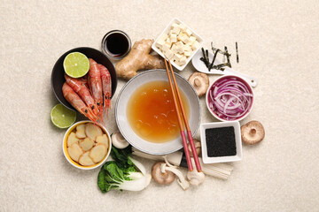 Fototapeta na wymiar Cooking delicious ramen soup. Different fresh ingredients in bowls and chopsticks on beige table, flat lay