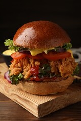 Delicious burger with crispy chicken patty on wooden table, closeup