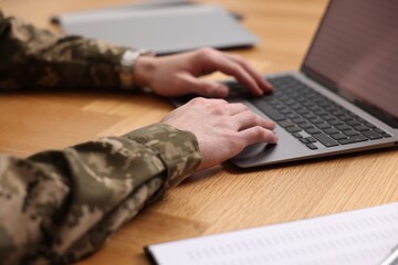 Military service. Soldier working with laptop at wooden table, closeup