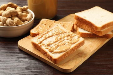Delicious toasts with peanut butter and nuts on wooden table, closeup