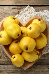 Naklejka na ściany i meble Tasty ripe quinces in heart shaped bowl on wooden table, top view