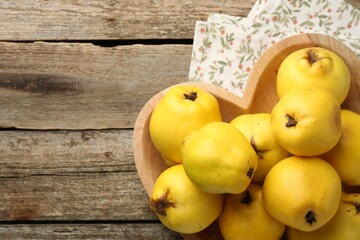 Tasty ripe quinces in heart shaped bowl on wooden table, top view. Space for text