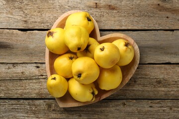 Tasty ripe quinces in heart shaped bowl on wooden table, top view