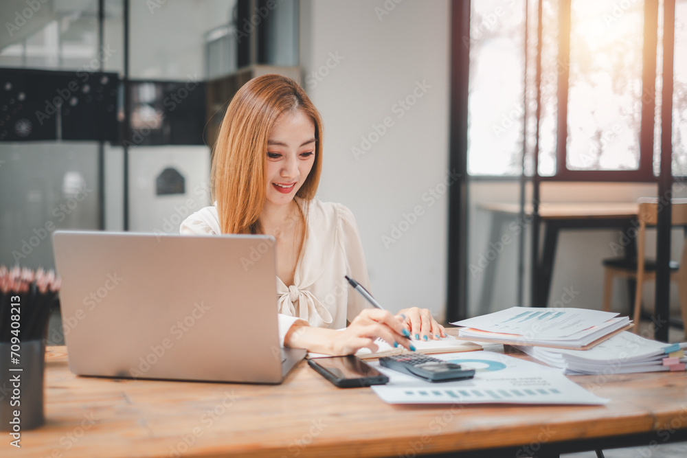 Poster smiling young woman using calculator and laptop computer to calculate financial report, working at o