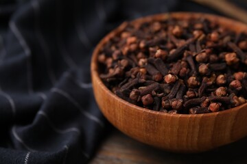 Aromatic cloves in bowl on wooden table, closeup. Space for text