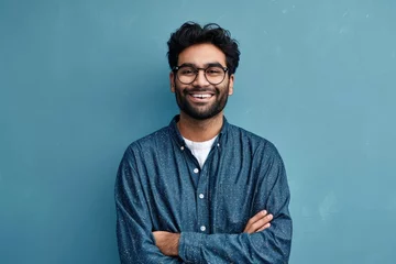 Foto op Canvas Smiling confident arab young man, male student, professional employee or programmer standing isolated on blue background. Happy handsome ethnic guy wearing shirt and glasses, Generative AI  © Geetanjali