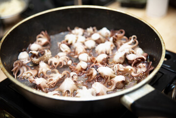 Sautéed Baby Octopus in Pan Close-up. Fresh baby octopus being sautéed in a large frying pan, showcasing a close-up of the cooking process.