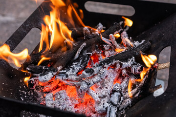 Close up of campfire, fire pit filled with burnt wood, flames. Fire burning, embers glowing.