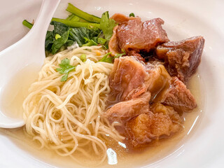 Closeup and crop Chinese eggs noodle with stewed meat soup in white ceramic bowl.