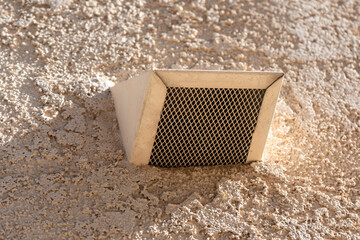 Exterior wall air vent on beige stucco wall.