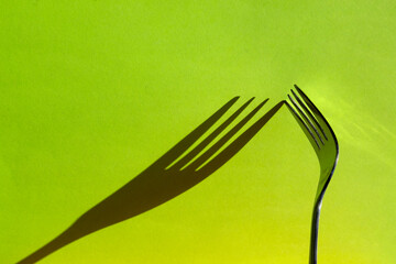 Indoor studio shot of the shadow of the tines of a fork on a lime green plain background.