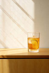 A Glass of Iced Tea with Lemon on Wooden Cabinet Composition. White Background. Natural Lighting and Shadow. Minimalist Photo. Minimal Modern Interior. Summer Beverage. 