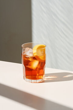 A Glass of Iced Tea with Lemon on White Counter. Artistic Corner Composition. White Background. Bright Lighting and Long Shadow. Minimalist Photo. Minimal Modern Interior. Summer Beverage.