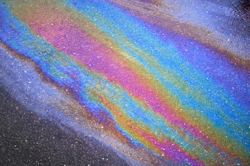 Background texture of an oil spill in the form of a rainbow stain on dark asphalt, parking