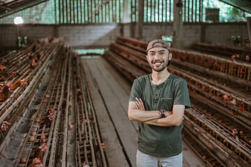 smiling young Asian entrepreneur with crossed hands standing on a chicken farm