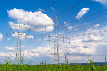 Electricity pylons with high voltage lines on the grass field in the landscape