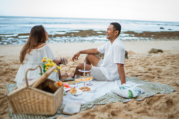 newlywed couple sitting on a picnic blanket chatting during a picnic at the beach