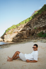 Naklejka na ściany i meble young Asian man in white shirt with sunglasses lying on a tropical beach