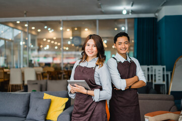 male and female waitress in apron hold a tab standing in front of couch in furniture store...