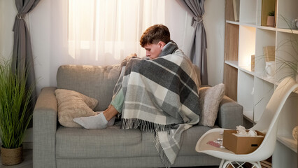 Virus infection. Sick man. Home health treatment. Bad feeling guy wrapped in blanket sitting on...
