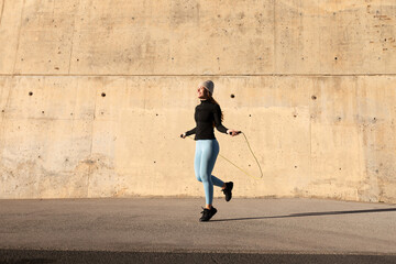 Female doing cardio workout. Woman in sports clothes jumping the rope. Rope skipping outdoors exercising. Copy space.
