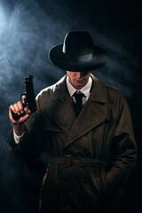 Silhouette of a male detective in a coat and hat with a gun in his hands. A dramatic noir portrait in the style of books and detective films of the 1950s.