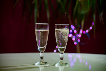 Pouring of brut champagne, cava or prosecco wine in glasses with garland lights on dark background, new year or birthday party