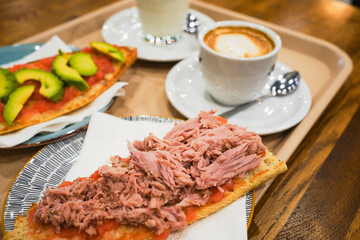 A close-up of tuna on toast, with coffee and milk in the background.