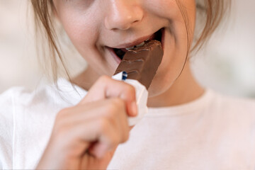 A girl bites a chocolate bar with her teeth in close-up. The harm of sweets for teeth. Addiction of...