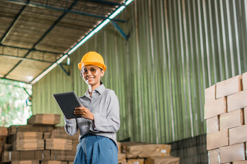 smiling female factory worker wearing safety helmet standing holding a tablet in a warehouse