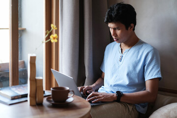 Asian man wearing casual outfit looking serious while checking mail, news, social networks, working on notebook, writing blog, studying at home, resort, hotel on weekend. Online freelance concept.