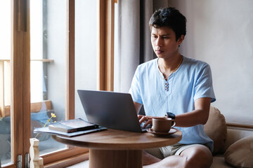 Asian man wearing casual outfit looking serious while checking mail, news, social networks, working...