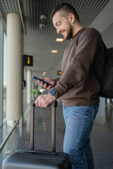 Busy tourist man locating in waiting hall. Young man with cellphone at the airport while waiting for plane