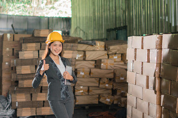 smiling young businesswoman wearing safety helmet holding a tab with thumbs up in warehouse