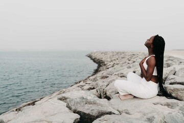 Woman with braids sittingon the rocks at the beach meditating