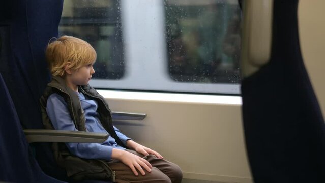 Cute preteen boy is traveling in a local train carriage or by railroad while it rain outside. Portrait of child passenger.