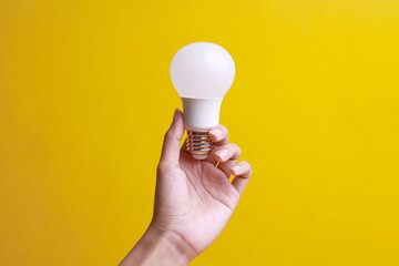 Hand holding a light bulb LED isolated over yellow background. Concept of saving energy and...
