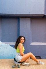 Fototapeta na wymiar Asian woman sitting on her skateboard next to the blue wall