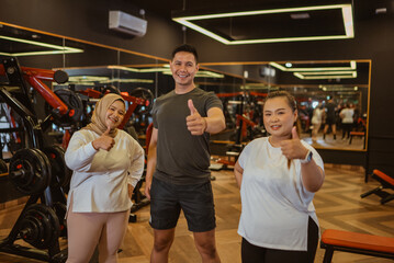 gym instructor and trainee standing with thumb up gesture in gymnasium