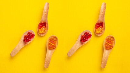 Jelly bears candy in wooden spoon, gummy bear on yellow background
