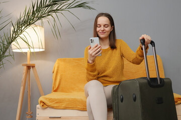 Attractive Caucasian business woman wearing orange sweater sitting with baggage on couch in hotel...