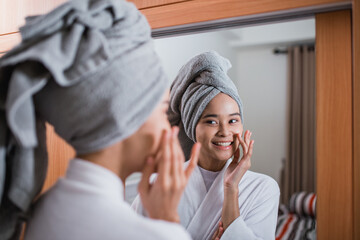 smiling girl wearing bathrobe and towel with fingers touching cheeks reflecting in bathroom - obrazy, fototapety, plakaty