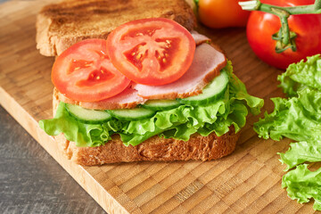 Sandwich with ham, lettuce, tomato and cucumber on wooden board
