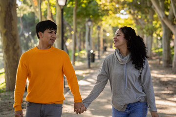 Happy young latin couple holding hands at park and looking at each other. - obrazy, fototapety, plakaty