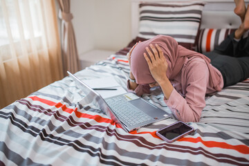 woman in veil dizzy while using laptop while lying on bed in room