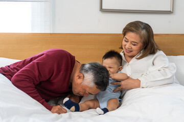 Obraz premium Portrait of happy love asian grandfather with grandmother playing with asian baby on bed, senior, insurance.Big family love with their laughing grandparents smiling together.Family and togetherness